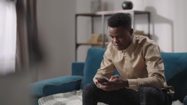 Yalnız bir Afro-Amerikalı dairede oturuyor, akıllı telefon kullanıyor, internet sitelerine bakıyor, sosyal ağlara bakıyor, erkek kullanıcı