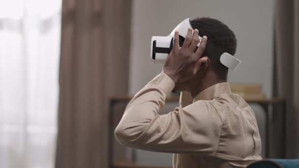 Joven afroamericano está posponiendo la pantalla montada en la cabeza y mirando la realidad, usando gafas vr en casa — Vídeos de Stock