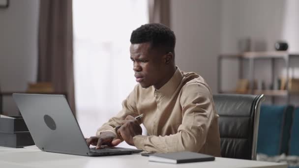 Üzgün Afro-Amerikalı adam merkez ofiste dizüstü bilgisayar kullanıyor, programın hatasını ve hatasını buluyor, yüzünü buruşturuyor, evde uzaktan çalışıyor. — Stok video