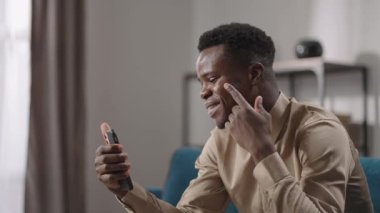 Neşeli genç Afro-Amerikalı adam cep telefonuyla cep telefonuyla konuşuyor, gülüyor ve ön kamerayla konuşuyor.