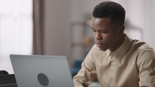 Negro estudiante masculino está estudiando en línea, sentado en la computadora portátil delantera en la habitación y el envío de mensajes en el chat, examen en línea — Vídeo de stock