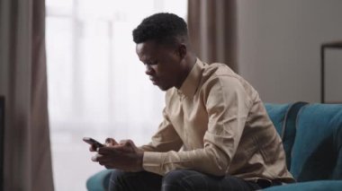 Genç adam apartmanda oturuyor ve akıllı telefon kullanıyor. Afro-Amerikalı adam internette cep telefonuyla dolaşıyor. Hafta sonları tek başına dinleniyor.