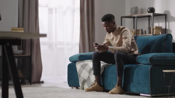 Jonge zwarte man speelt videospel in smartphone, zitten thuis alleen, afro-Amerikaanse man communiceert in sociale netten in mobiele telefoon — Stockvideo