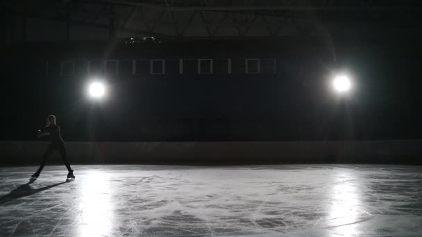 Jovem patinadora figura feminina está vestindo sportswear preto para treino está patinando na pista de gelo sozinho à noite, treinamento — Vídeo de Stock