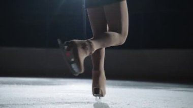 tek kadın artistik patinaj performansı, buz pistinde dönen elementler sırasında spor kadınlarının bacaklarına yakın çekim, yarışma ve gösteri performansı
