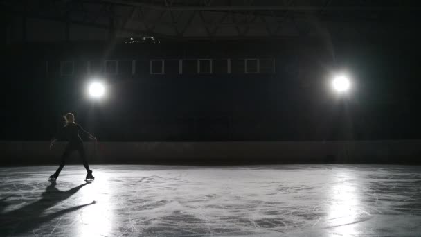 Pattinatrice a figura singola sta eseguendo elementi durante l'allenamento sulla pista di pattinaggio sul ghiaccio di notte, duro allenamento per i futuri campioni — Video Stock