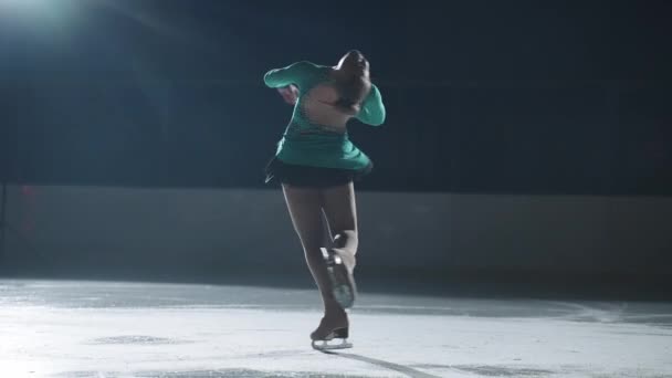 Молодая фигуристка вращается на льду в темноте, соревнованиях и показательных выступлениях спортсменки — стоковое видео