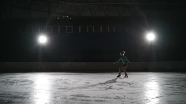 Jovem patinadora artística feminina está realizando salto duplo ou triplo no gelo, patinando sozinha na escuridão, treinando à noite — Vídeo de Stock