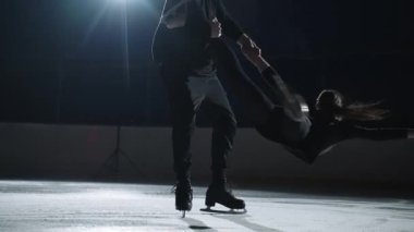 Erkek ve kadın artistik patinaj kaldırma ve döndürme gösterisi yapıyorlar, profesyonel çift patenciler buz pistinde antrenman yapıyor, erkek kadını tutuyor ve dönüyor.