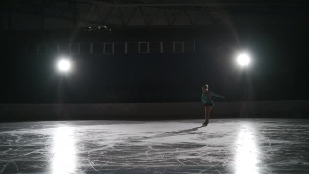 Junior solo patinador artístico femenino está entrenando en pista de hielo, ejercicio de salto y camello spin, calentamiento antes de la actuación en el campeonato — Vídeos de Stock