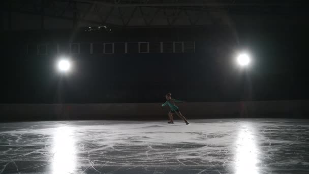 年轻的单身女子花样滑冰选手独自在黑暗的空荡荡的体育场训练，女孩独自在溜冰场滑冰 — 图库视频影像