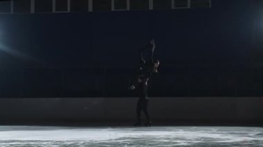 Artistik patinaj kaldırışı, buz pateni pistinde iki patenci, erkek kadını omuzlarında tutuyor, ağır çekimde profesyonel antrenman yapıyor.