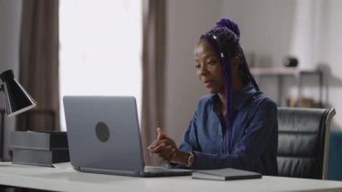 Genç siyahi kadın laptopta görüntülü sohbet yoluyla iletişim kuruyor, müşterisiyle ya da iş arkadaşıyla sohbet ediyor.