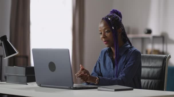 Молодая черная женщина общается посредством видеочата на ноутбуке, общаясь с клиентом или коллегой из своего домашнего офиса — стоковое видео