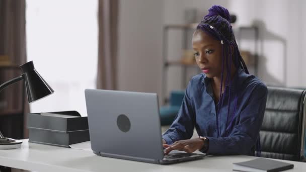 Mulher afro-americana está trabalhando com laptop, trabalho remoto em casa, jovem está sentada à mesa e enviando e-mail — Vídeo de Stock