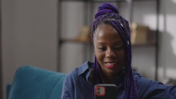 Affascinante giovane donna africana sta guardando video in smartphone e sorridente, a riposo a casa durante il fine settimana — Video Stock