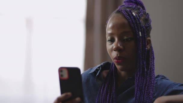 Chamada de vídeo no smartphone moderno, jovem mulher negra está se comunicando com alguém, sentado em casa, olhando para exibição e conversando — Vídeo de Stock