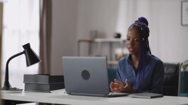 Bilgisayarla video bağlantısı kuran siyahi kadın, uzak iş görüşmeleri sırasında iş arkadaşlarıyla konuşuyor, evden çalışıyor.