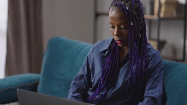 Afro-americká žena hacker nebo programátor pracuje s notebookem doma, sedí na gauči v místnosti a psaní na klávesnici — Stock video