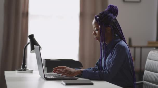 Adulto mulher negra está aprendendo on-line em casa, sentado à mesa com laptop, digitando no teclado, retrato — Vídeo de Stock