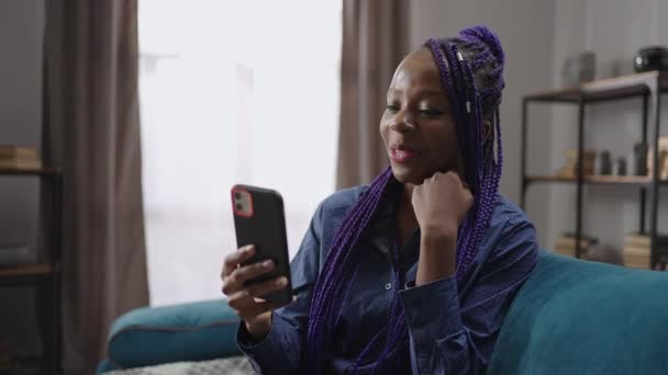 快乐的非洲裔美国女人正在社交网络上看搞笑视频，使用智能手机，在家里休息 — 图库视频影像