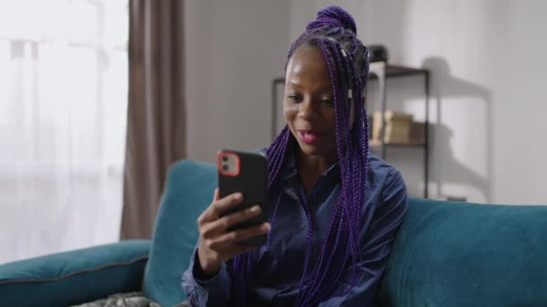 Happy afro-amerikaanse jonge vrouw is het bekijken op het scherm van haar smartphone en glimlachen, communiceren door middel van video call — Stockvideo