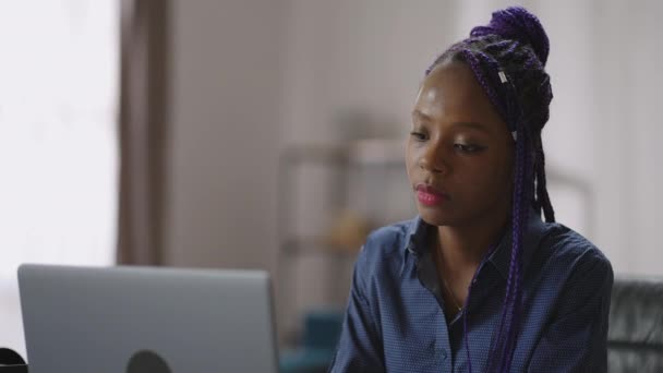 Portret van jonge afro-Amerikaanse vrouw met paarse dreadlocks aan tafel met laptop, zwarte dame is met behulp van internet — Stockvideo