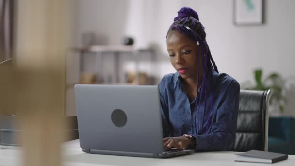 Афроамериканка работает дома с ноутбуком, удаленная работа в домашнем офисе, молодая чернокожая дама серфингует в Интернете — стоковое видео