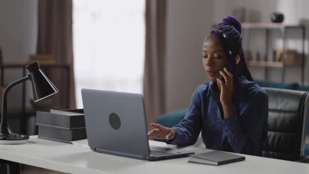 Młoda kobieta pracuje w biurze domowym, dzwoni przez telefon komórkowy, siedzi przy stole z laptopem, sprawdza informacje, portret pracowniczki — Wideo stockowe