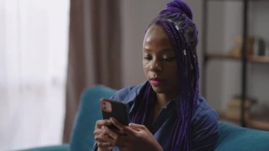 Nijeryalı öğrenci bayan evde haberciyle akıllı telefon kullanıyor. Rasta saçlı güzel bir genç kadının portresi.