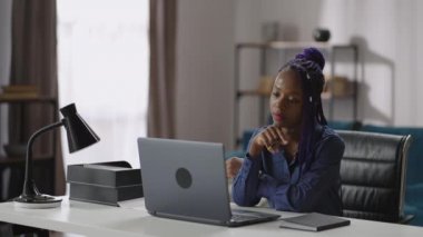 Afro-Amerikalı bir kadın dizüstü bilgisayar ekranına bakıyor ve web sitesi ya da internet konferansı öğreniyor.