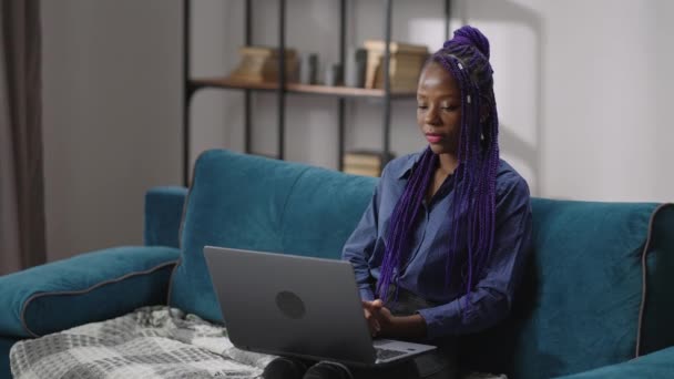 Дистанционное собеседование для молодой черной женщины по видео-конференции в ноутбуке, женщина сидит на диване и держит ноутбук на коленях — стоковое видео