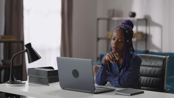 Афроамериканка смотрит на экран ноутбука и слушает обучающий веб-сайт или онлайн-лекцию — стоковое видео