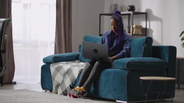 Single afro-amerikaanse vrouw is met behulp van laptop, alleen thuis zitten in het weekend, zitten op de bank in de kamer en surfen op internet — Stockvideo