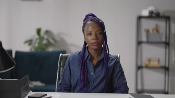 보라색 레게 머리를 하고 현대적 인 머리 스타일의 젊은 흑인 여성의 사진,아 프로 - 미국 여성 아파트에 테이블에 앉아 카메라를 보고 — 비디오