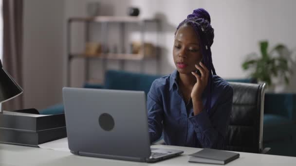 Kvinnlig försäljningschef arbetar på hemmakontoret, svart kvinna ringer via mobiltelefon, sitter vid bord med laptop, konsulterar kunder — Stockvideo