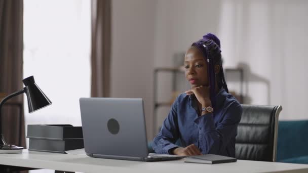 Giovane donna afro-americana con acconciatura moderna sta guardando video presentazione o film in mostra di laptop, seduto a tavola a casa o in ufficio — Video Stock