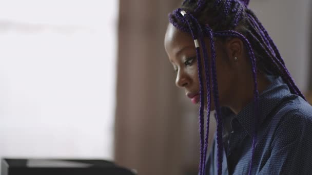 Ενήλικη αφρο-αμερικανική γυναίκα με μωβ dreadlocks εργάζεται με φορητό υπολογιστή στο γραφείο στο σπίτι, απομακρυσμένη δουλειά στο σπίτι, νεαρή μαύρη κυρία στέλνει e-mail — Αρχείο Βίντεο