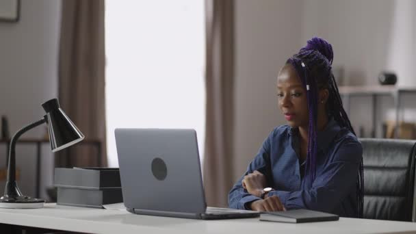 Portrét mladé černošky s fialovými dredy u stolu s laptopem, africká americká dáma prohlíží video na displeji, online setkání nebo konferenci — Stock video