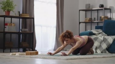 Kadın evde yoga egzersizleri yapıyor, oturma odasında tek başına antrenman yapıyor, sağlığa önem veriyor, asana egzersizleri yapıyor.