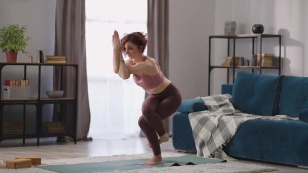 在家里做瑜伽训练，女人站在花冠上，女士做鹰的姿势，锻炼保持平衡，保持健康 — 图库视频影像