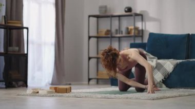 Kadın evde fiziksel egzersiz yapıyor, yoga asanası yapıyor, omurilik eğitimi alıyor, osteokondrosisin önüne geçiyor.