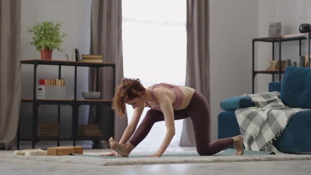 Mujer deportiva adulta está realizando asana para estirar las piernas, practicar hatha yoga en casa, entrenamiento matutino, estilo de vida saludable — Vídeos de Stock