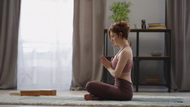 Erwachsene Frau meditiert zu Hause, sitzt in Lotusposition auf dem Boden im Wohnzimmer, praktiziert Yoga und Atemübungen — Stockvideo