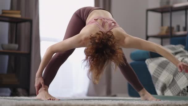 Femme sportive adulte étire le corps pendant l'exercice du matin, séance d'entraînement dans le salon, la femme abaisse la tête au sol — Video