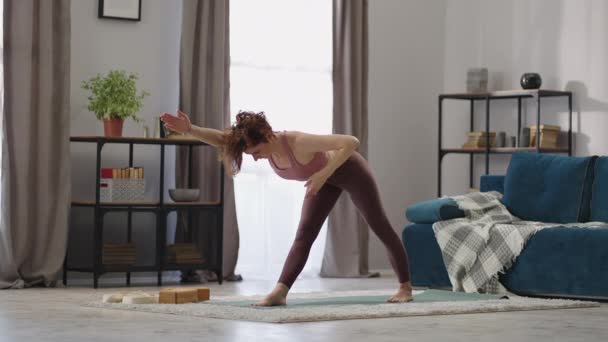 Vuxen sportig kvinna utför yoga asana i vardagsrummet, fysisk träning på morgonen träning, sport aktivitet — Stockvideo