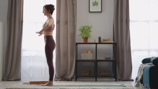 Joven deportista está entrenando yoga posición en sala de estar, haciendo ejercicio físico por la mañana, actividad deportiva — Vídeos de Stock