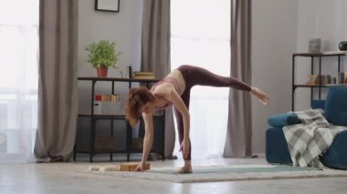 Kadın hatha yoga yapıyor, evde tek başına antrenman yapıyor denge için egzersiz yapıyor, tek ayak üzerinde duruyor.