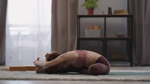 Vuxen kvinna tränar ensam hemma på morgonen, dam sträcker kroppen, sitter på golvet, full längd — Stockvideo