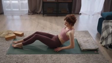 Kadın oturma odasında shavasana yapıyor, evde tek başına antrenman yapıyor, antrenmandan sonra dinleniyor, sağlıklı bir yaşam tarzı.